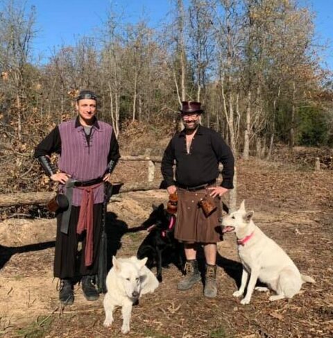Two Viking men and two white dogs standing in woods